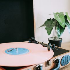 A pink record playing on a white suitcase turntable beside a plant