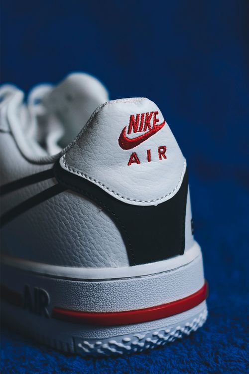 Free Detailed close-up of a white Nike Air Force 1 sneaker with red accents on a blue background. Stock Photo