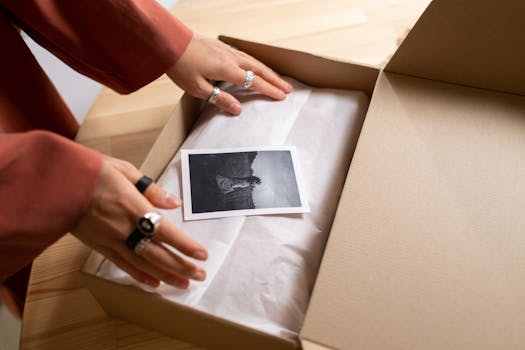 Hands opening a cardboard box revealing a photograph wrapped in tissue paper.