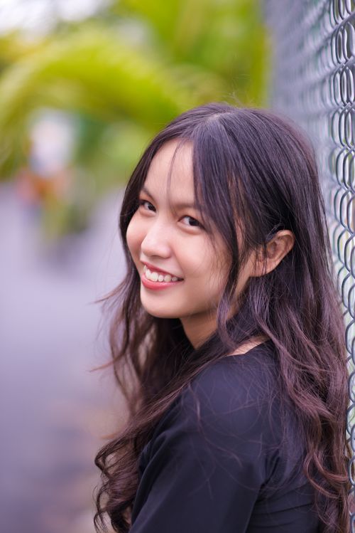 Free A cheerful young woman with long hair leans against a chain-link fence outdoors. Stock Photo