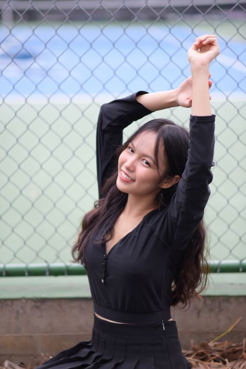 Free Cheerful woman in black outfit smiling and posing by a chain link fence outdoors. Stock Photo
