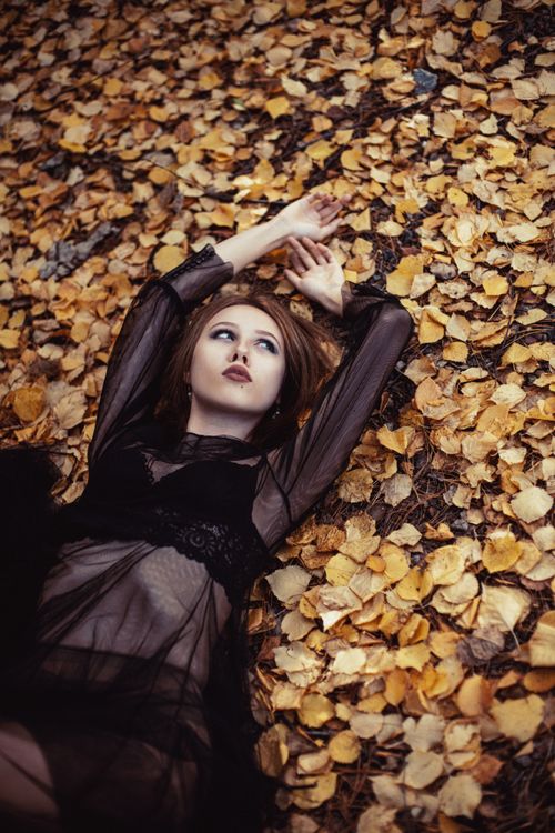 Free Young woman in black dress lying amidst golden fallen autumn leaves. Stock Photo