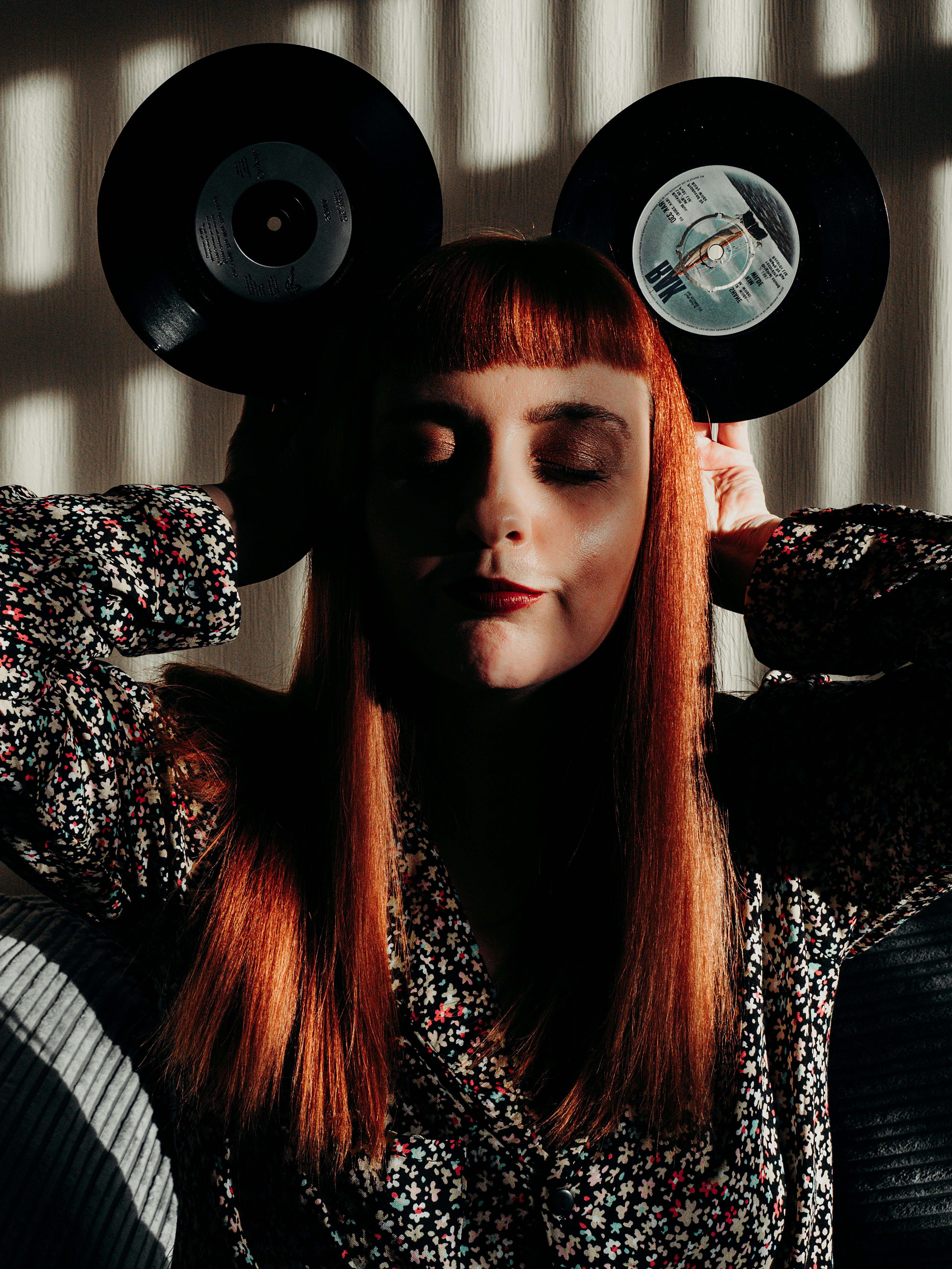 red hair woman with closed eyes holding vinyl records as mouse ears