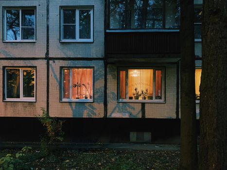 Exterior view of an apartment building with warmly lit windows on a cozy evening.