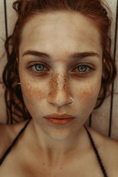 A detailed vertical close-up portrait of a freckled woman with striking eyes and a nose piercing.