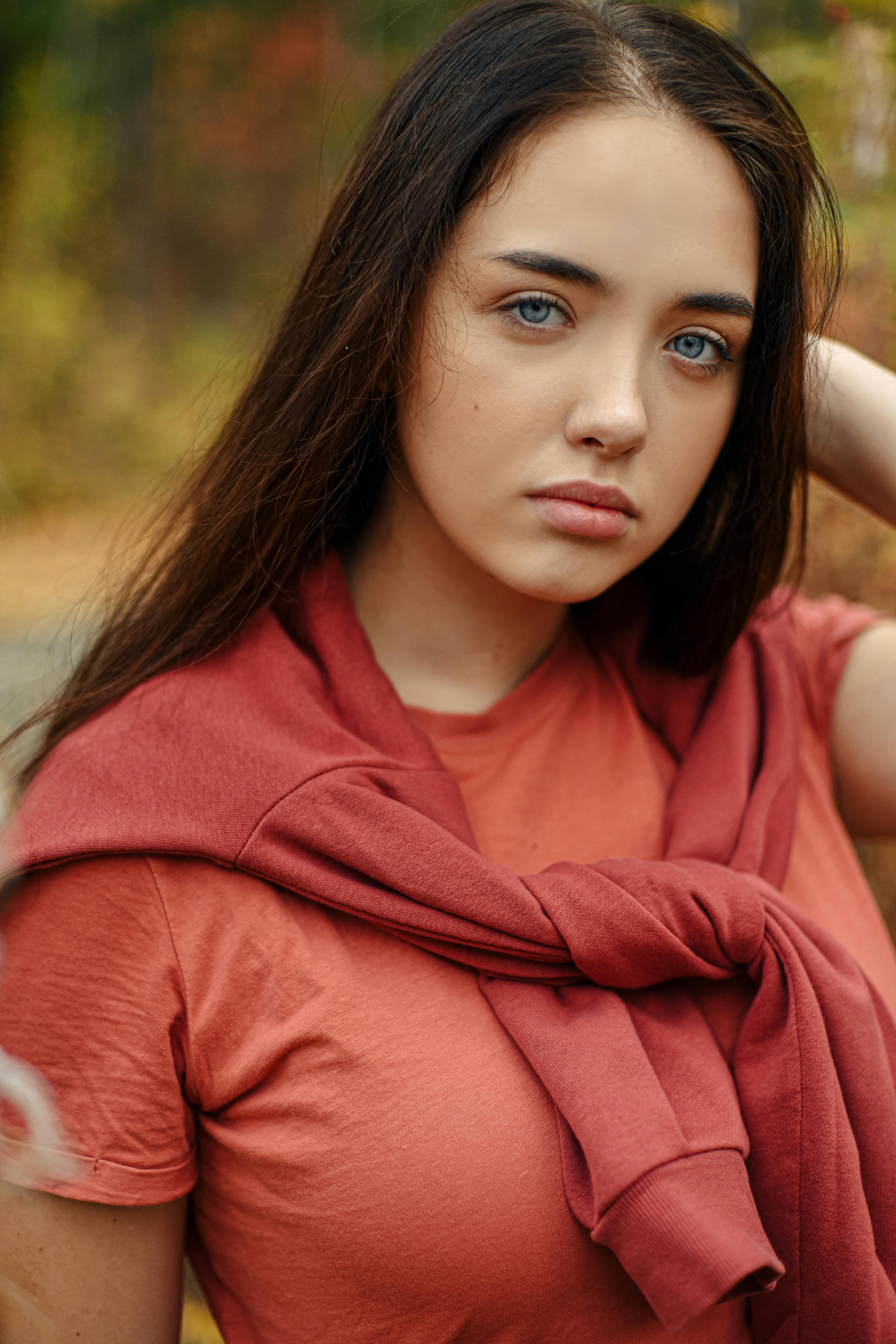 A young woman with striking blue eyes poses outdoors wearing a red shirt and sweater.