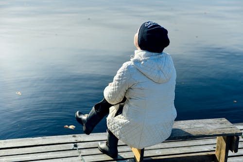 Woman in White Bubble Jacket Sitting on Wooden Bench