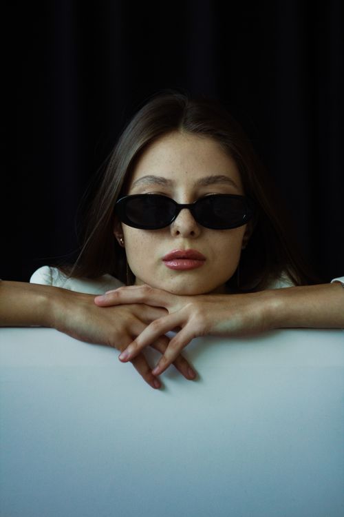 Free Portrait of a fashionable woman wearing sunglasses, posed against a dark backdrop. Stock Photo