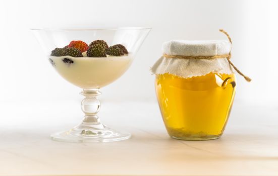 Chic glass filled with berries and cream alongside a jar of honey, perfect for food lovers.