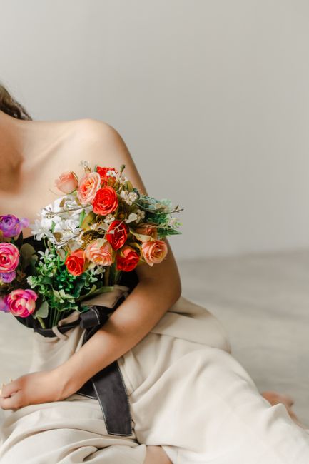 A woman in a stylish pose holding a vibrant bouquet of assorted flowers indoors.