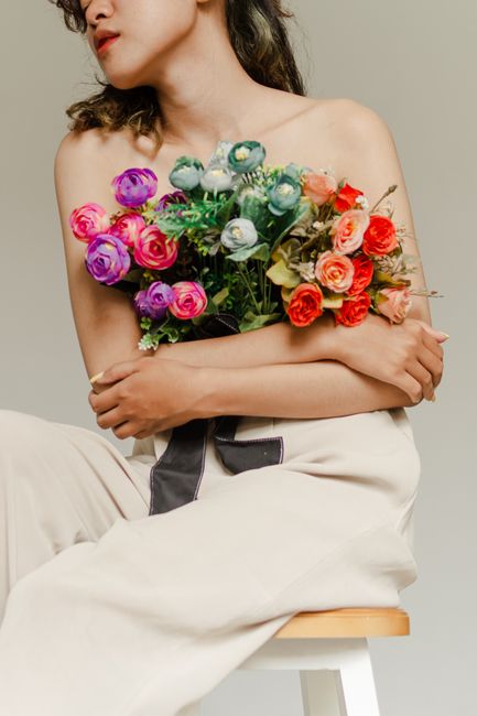 A woman poses subtly in a studio holding a colorful bouquet of flowers, embracing elegance.