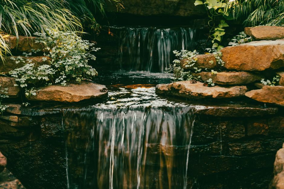 Peaceful scene of a lush garden waterfall surrounded by rocks and greenery, perfect for tranquil landscapes.
