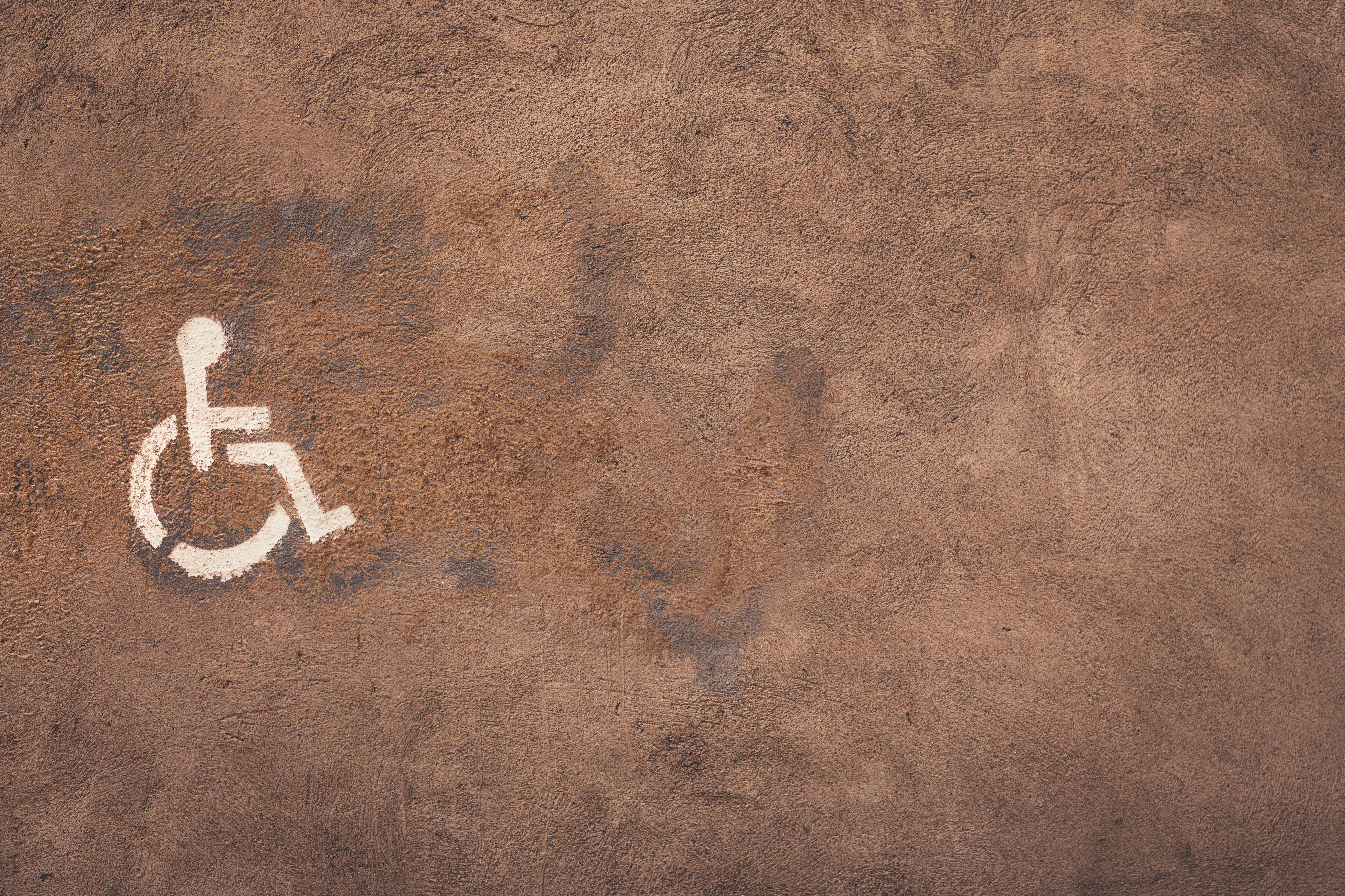 Brown concrete wall with painted wheelchair symbol indicating accessibility. Ample copy space.
