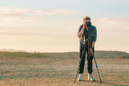 Man with a camera and tripod capturing scenic views in an open field at sunset.