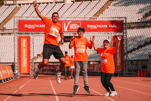 Free Cheerful family jumping for joy at the finish line of an outdoor race, wearing matching orange shirts. Stock Photo