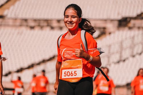 Free Smiling girl running in a marathon, giving a thumbs up, wearing a bright orange shirt. Stock Photo