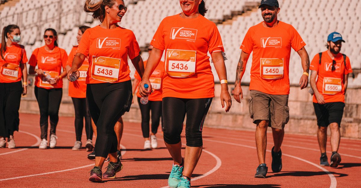 Group of people in bright orange shirts enjoying a walkathon on an outdoor track.