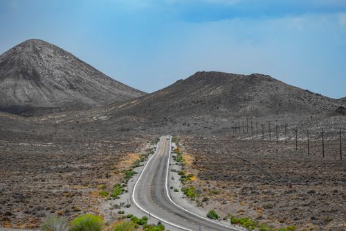 Free A solitary road traverses the rugged desert landscape of Tonopah, Nevada, under a vast blue sky. Stock Photo