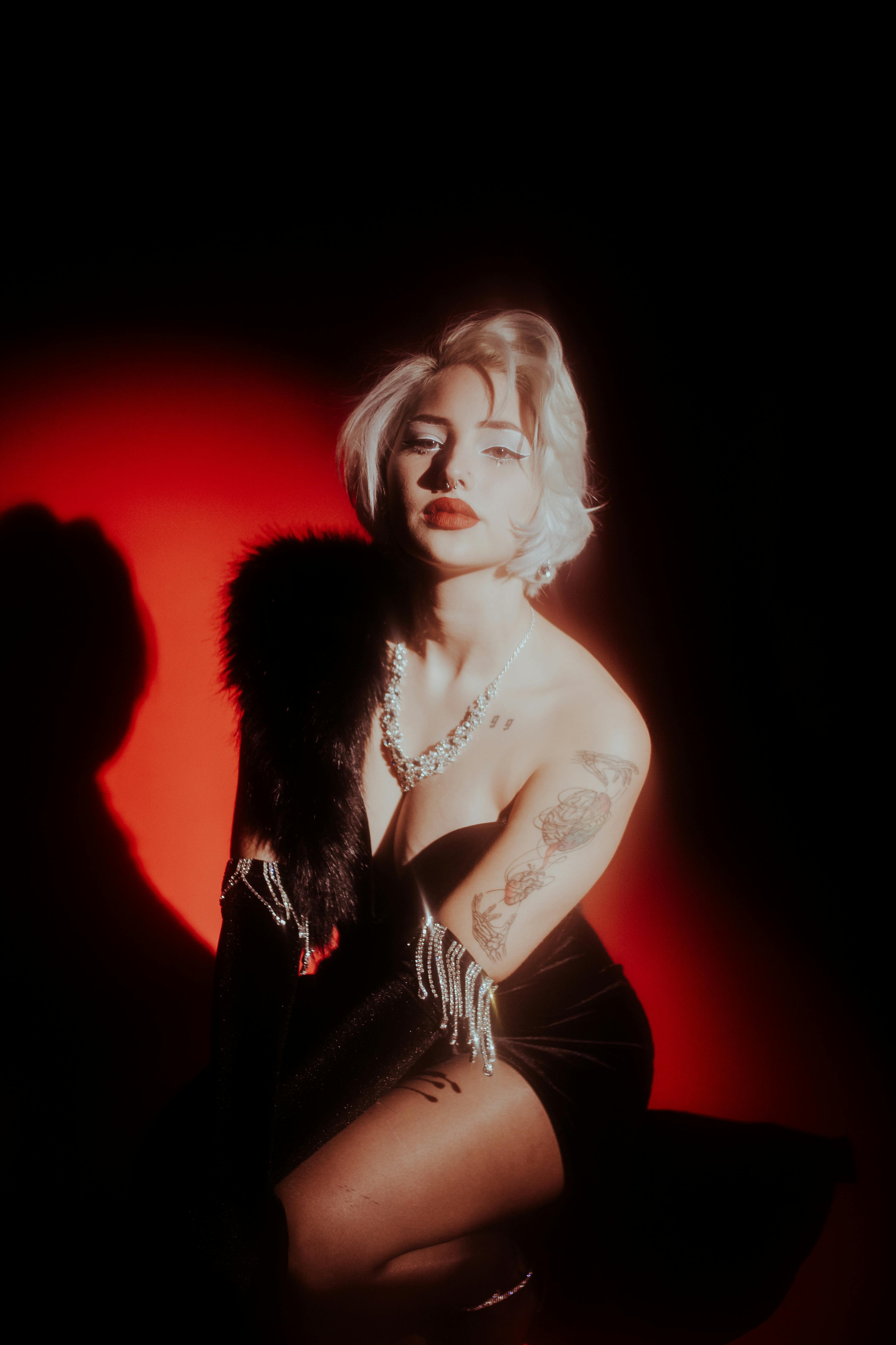Stylish woman with tattoos posing in dramatic lighting indoors, wearing evening wear.