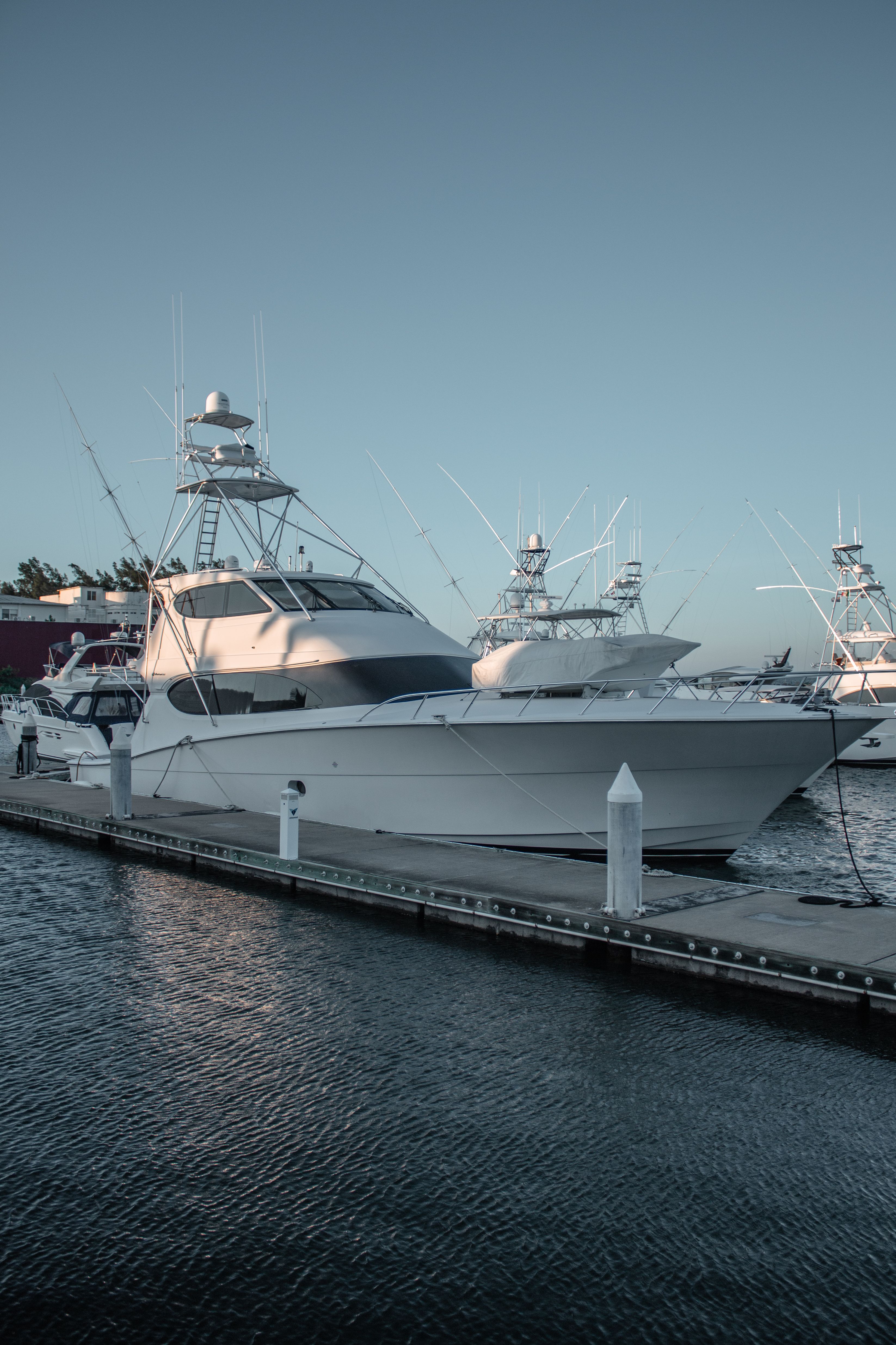 White glass-reinforced plastic boat hulls moored along a dock at dusk, their glossy gelcoat surfaces reflecting the pale sky.