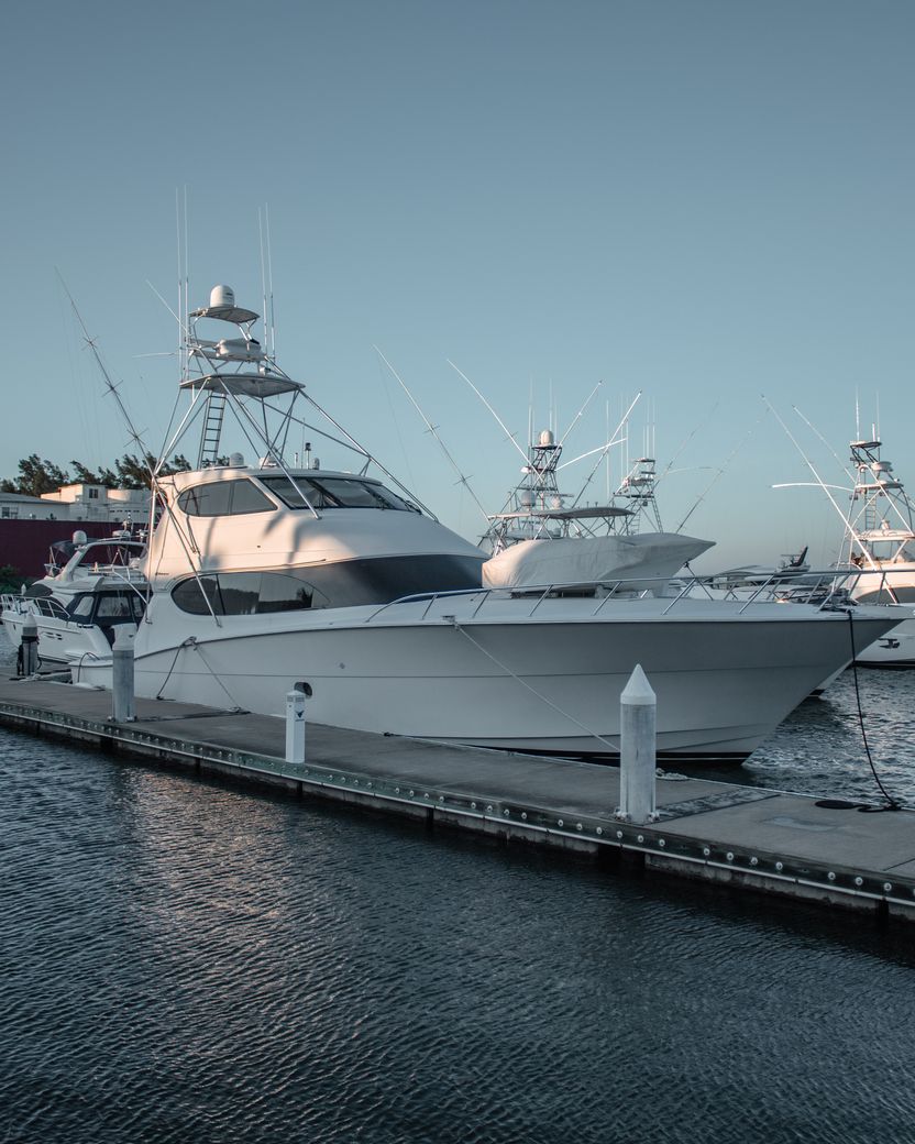 White glass-reinforced plastic boat hulls moored along a dock at dusk, their glossy gelcoat surfaces reflecting the pale sky.