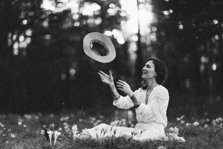 Woman Sitting On Grass Throwing Her Hat