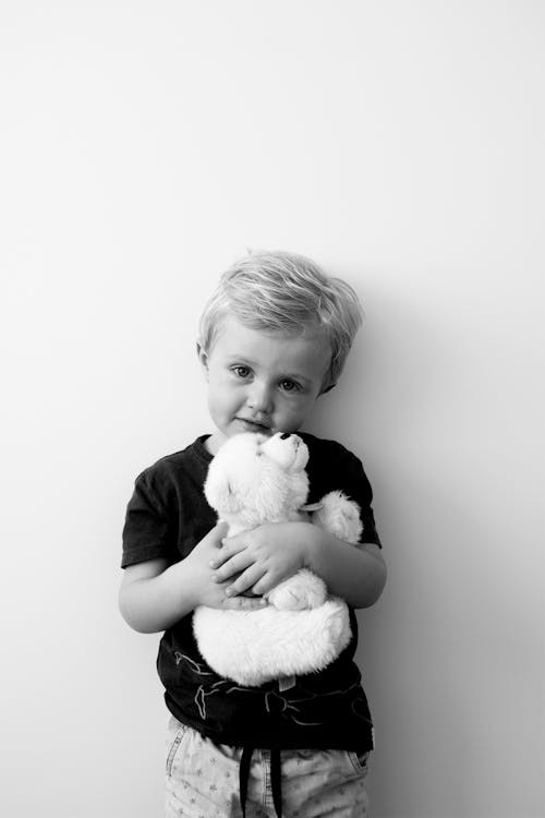 Free Grayscale Photo of Boy Holding Bear Plush Toy Stock Photo