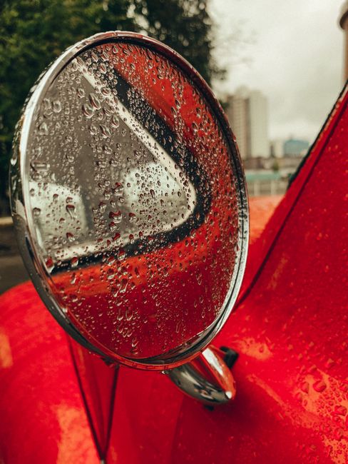 Raindrops on a classic car's side mirror with cityscape in the background.