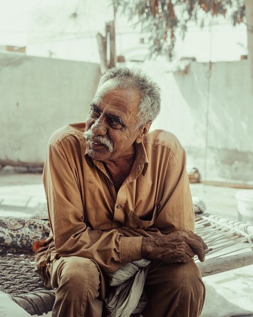 Free Portrait of an elderly man sitting outdoors in traditional clothing, exuding wisdom and warmth. Stock Photo