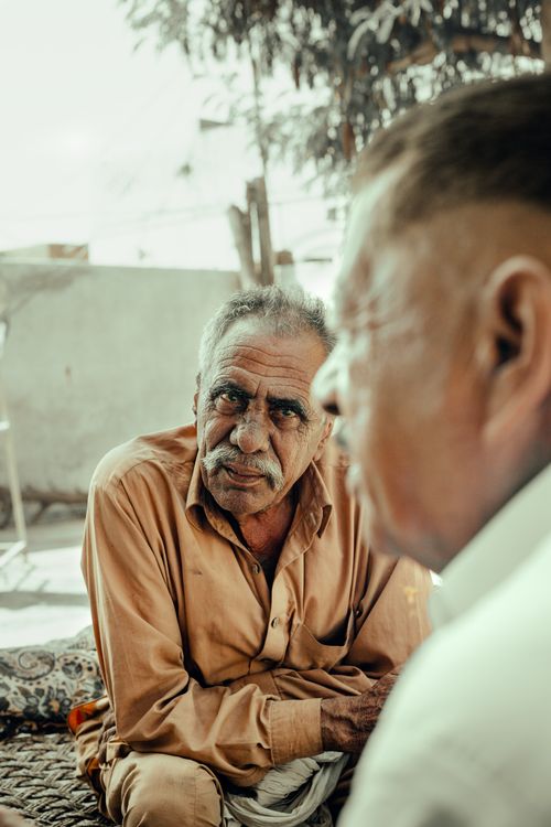 Free Elderly man with mustache conversing while sitting outdoors. Candid and expressive portrait. Stock Photo