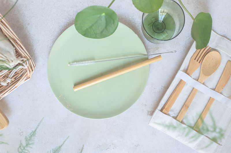 Flat lay of bamboo cutlery set with green plate and glass for sustainable dining.