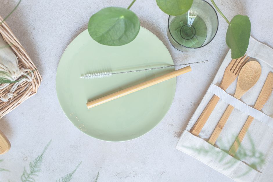 Flat lay of bamboo cutlery set with green plate and glass for sustainable dining.