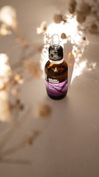 Brown cosmetic serum bottle in soft focus with gentle lighting and dried flowers, creating an elegant still life.