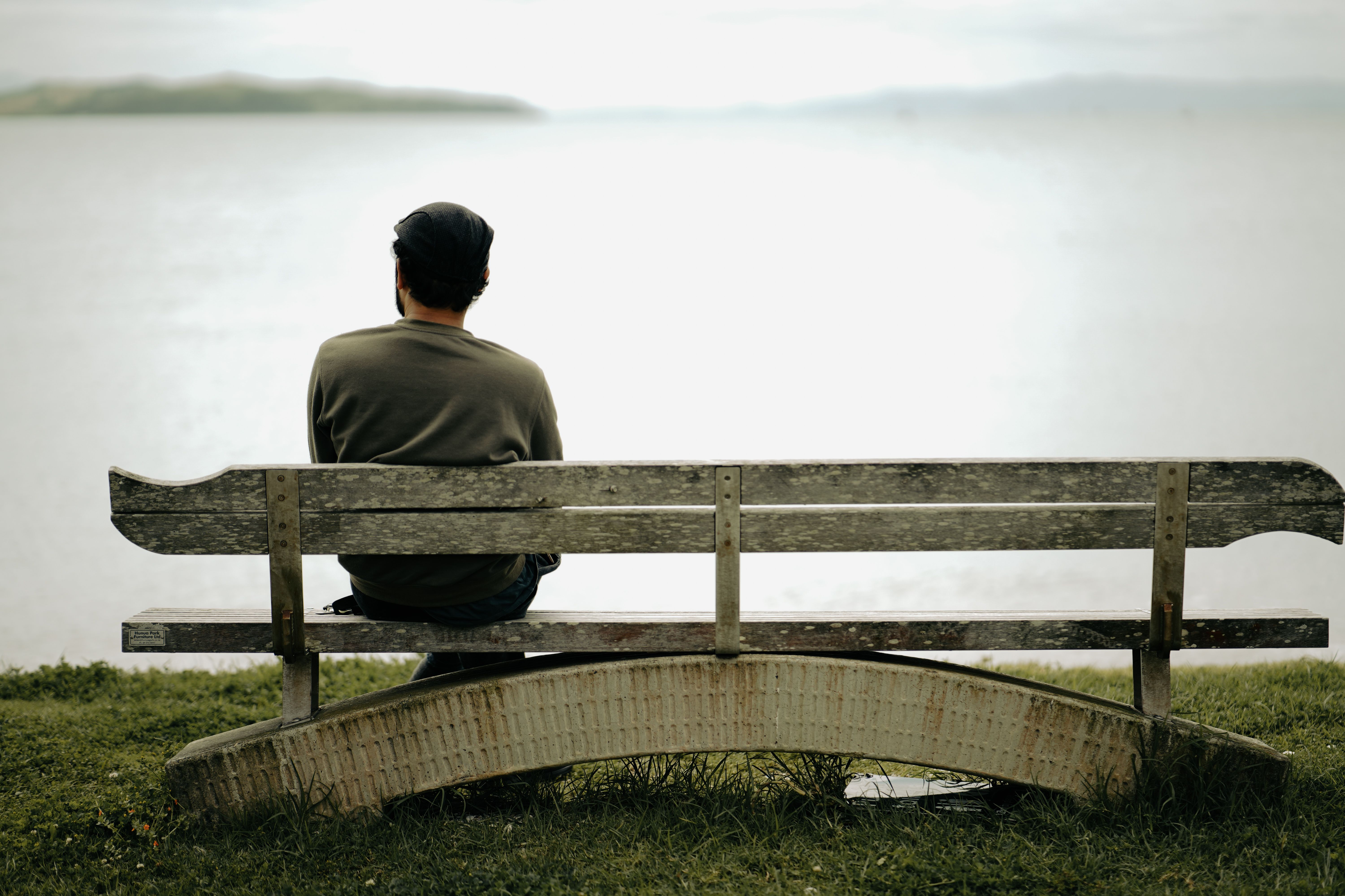 A person sits alone on a wooden bench by the water, capturing peaceful solitude.
