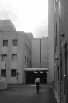 A man walks through a monochrome urban alley between tall buildings.