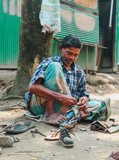 Free An artisan shoemaker working on a shoe outdoors surrounded by tools. Stock Photo