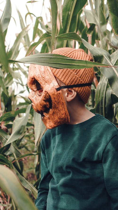 A Kid in Green Sweater Wearing a Scary Mask 