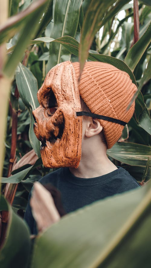A Kid in Orange Beanie Hat Wearing a Scary Mask 