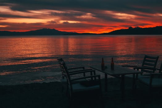 Dramatic sunset view with empty chairs and bottles by the calm seashore.