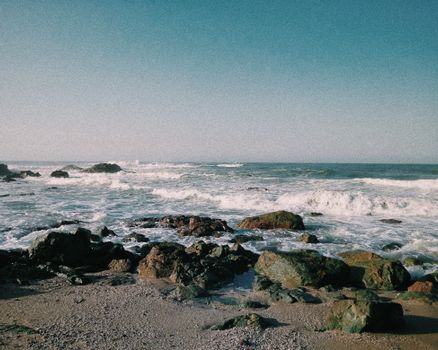 Vibrant beach landscape featuring rocks, waves, and a serene horizon under a clear sky.