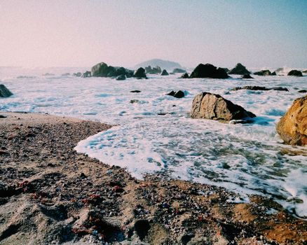 Scenic view of waves crashing on a rocky beach under a clear sky, perfect for nature photography enthusiasts.