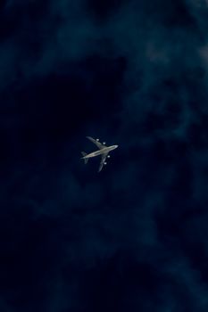 A commercial airplane captured mid-flight against a dark, moody sky.