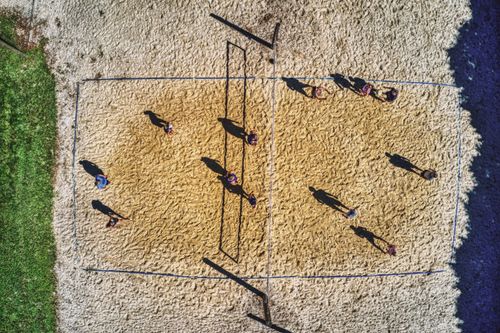 Free Drone shot capturing people playing volleyball on a sunny sand court. Stock Photo