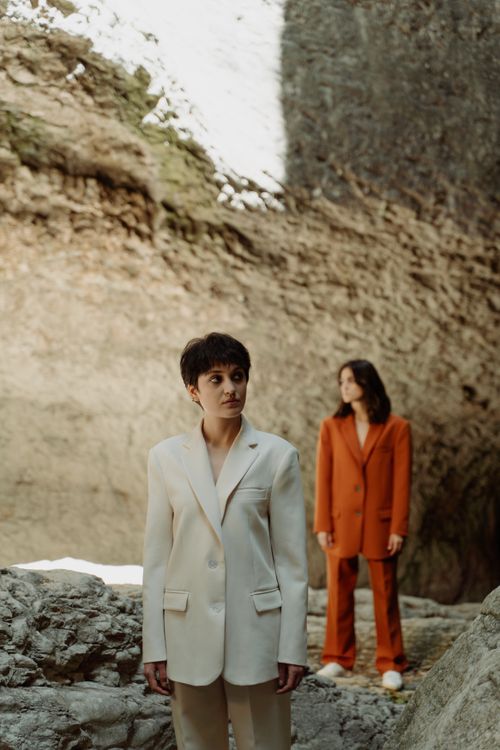 Free Stylish outdoor fashion shoot featuring two models in vibrant suits against a rocky backdrop. Stock Photo