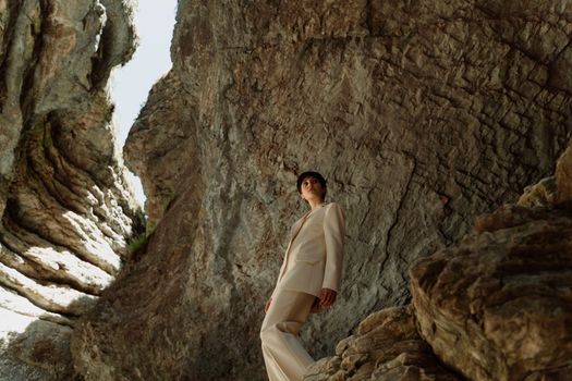 Stylish adult woman in a beige blazer posed within a dramatic cave scene.