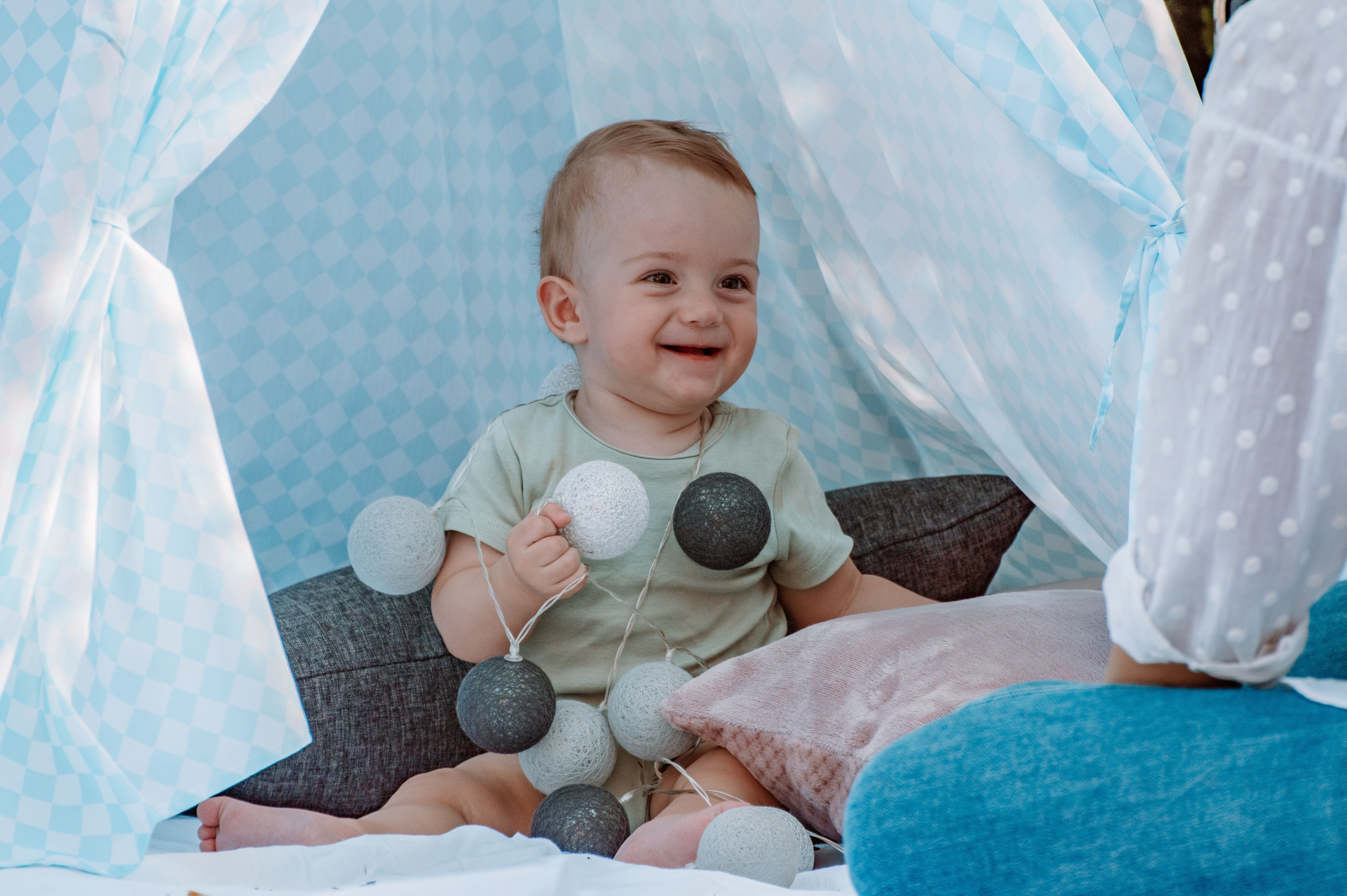 Smiling baby enjoying playtime in a cozy tent with string lights.