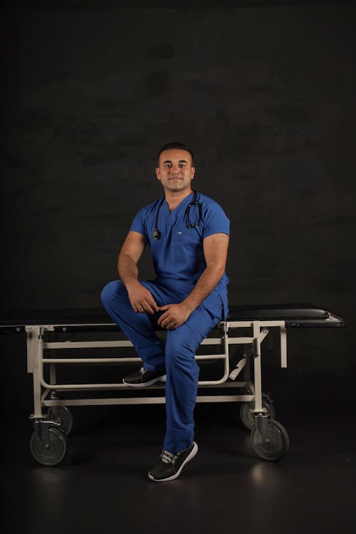 A Man Wearing a Scrub Suit Sitting on a Stretcher