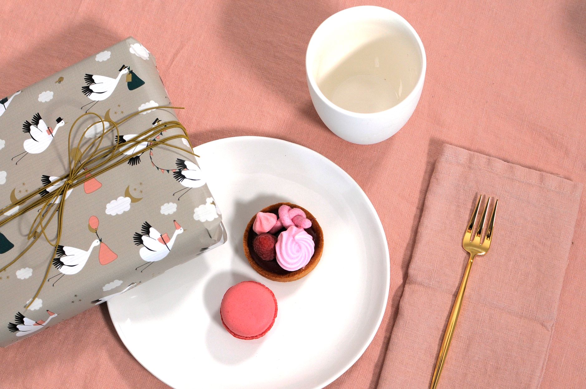 Festive setup with a wrapped gift, dessert plate, and pink macaron on a textured cloth.