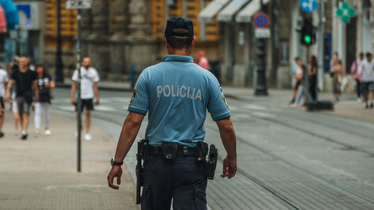 A police officer walking down a city street during the day, maintaining law and order.