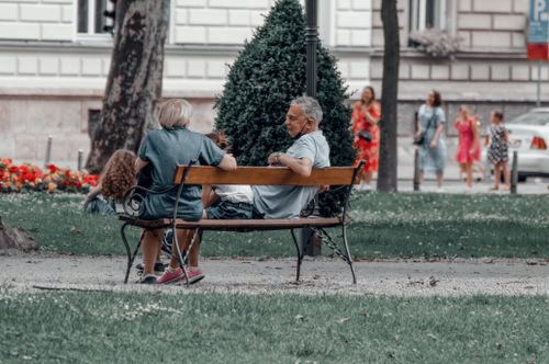 Free Two adults and a child enjoy a conversation on a wooden bench in a city park. Stock Photo